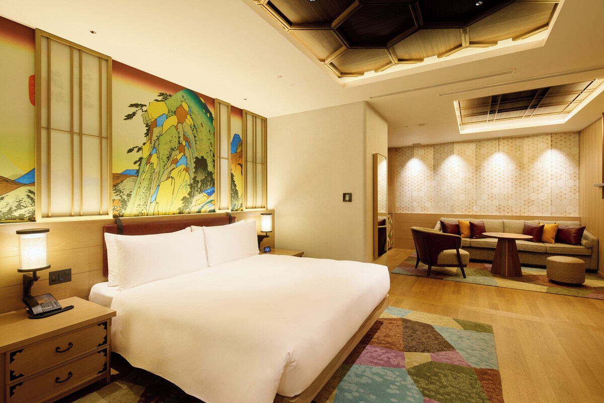 A hotel room with a large bed, a desk, and a sofa.
