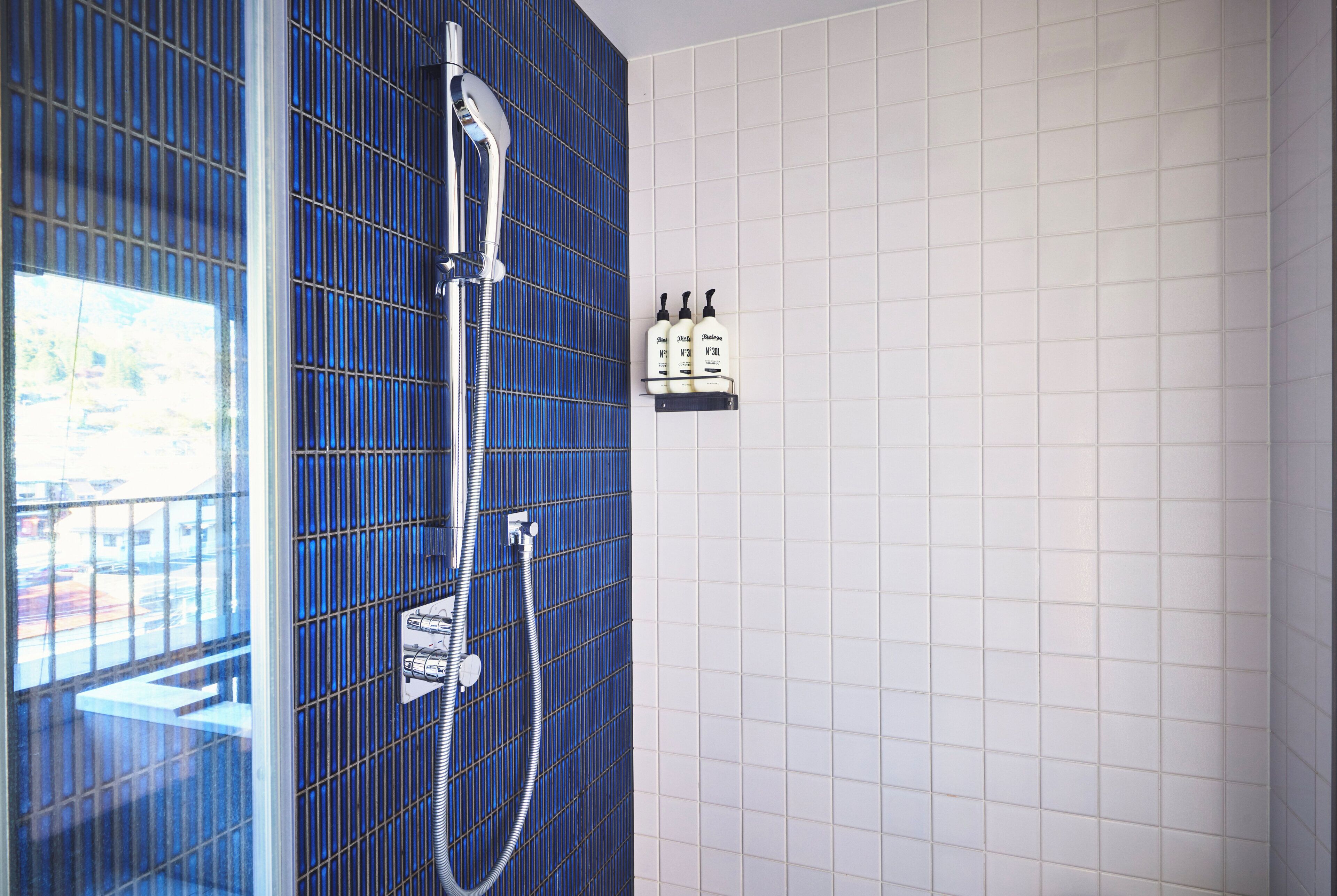 A bathroom with a blue tiled wall, a shower, and a shelf with toiletries.