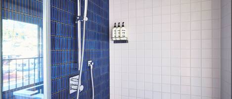 A bathroom with a blue tiled wall, a shower, and a shelf with toiletries.