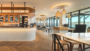 Zona de bar moderna con mostrador curvo, asientos y ventanas amplias con vista al mar.