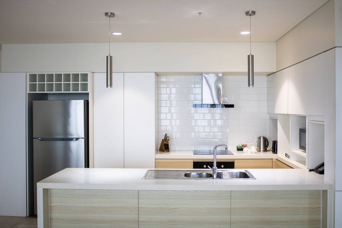 A modern kitchen with a stainless steel refrigerator, a double sink, and pendant lighting.