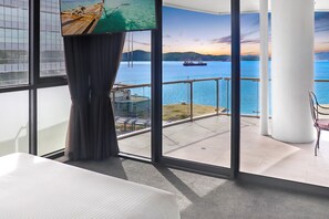A room with a large window overlooking a body of water, a balcony, and a view of a sunset. - Crowne Plaza Residences Port Moresby by IHG (Port Moresby)