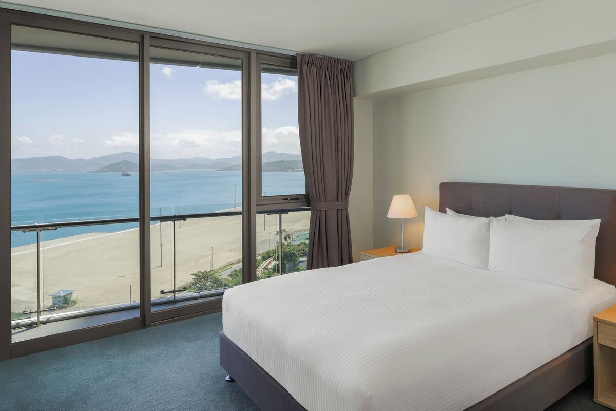A hotel room with a large window offering a view of the beach and ocean.