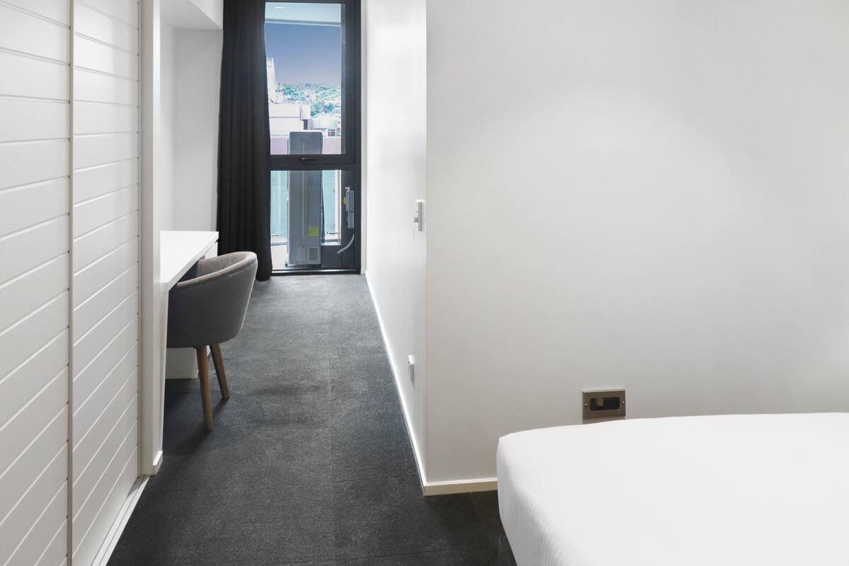 A hotel room with a bed, a desk, a chair, and a view of the outdoors through a window.