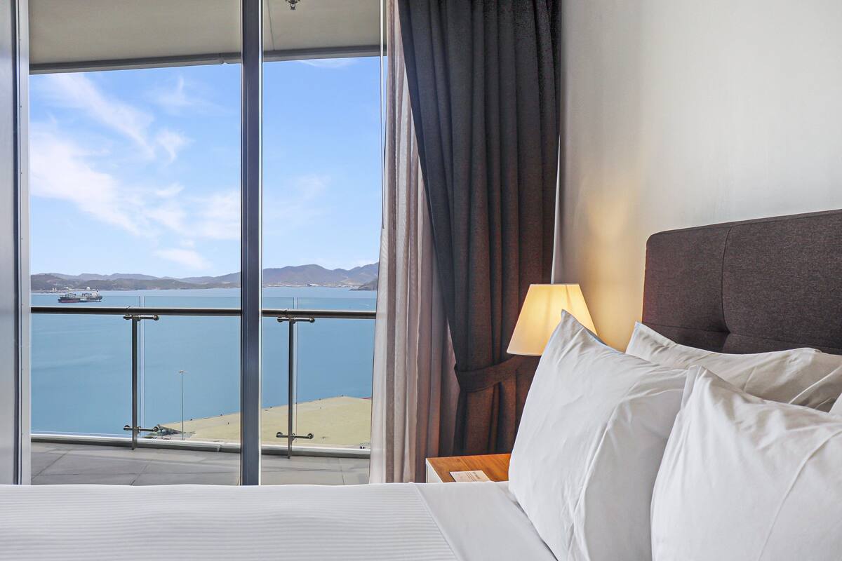 A hotel room with a large window offering a view of a body of water and distant land.