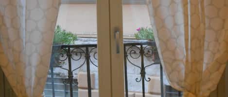 A window with a view of a balcony, curtains, and a metal railing.