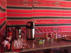 A kitchen counter with various items including a coffee maker, thermos, jars, and a tray with glasses.