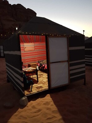 A tent with a striped exterior and a view of a bed with a red and white striped blanket. - Mohammed Camp (Wadi Rum)
