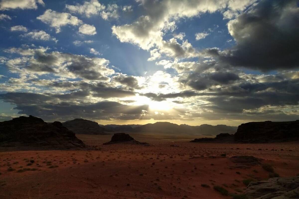 A desert landscape with a clear sky and sun setting or rising behind distant mountains.