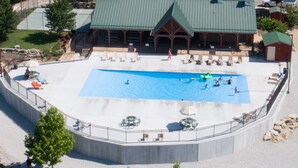 An aerial view of a swimming pool with a covered pavilion, lounge chairs, and a small building.
