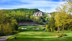 A golf course with bunkers, a clubhouse, and a forested hill in the background.