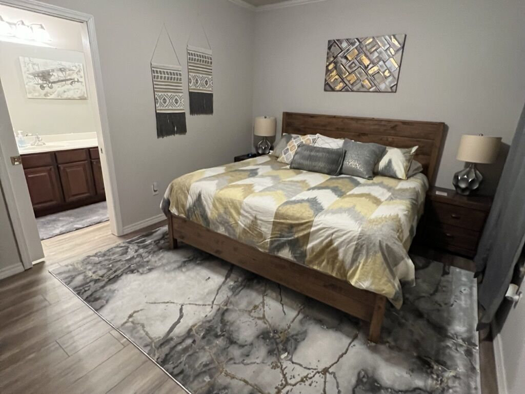A bedroom with a wooden bed, a marble-patterned rug, and wall art.