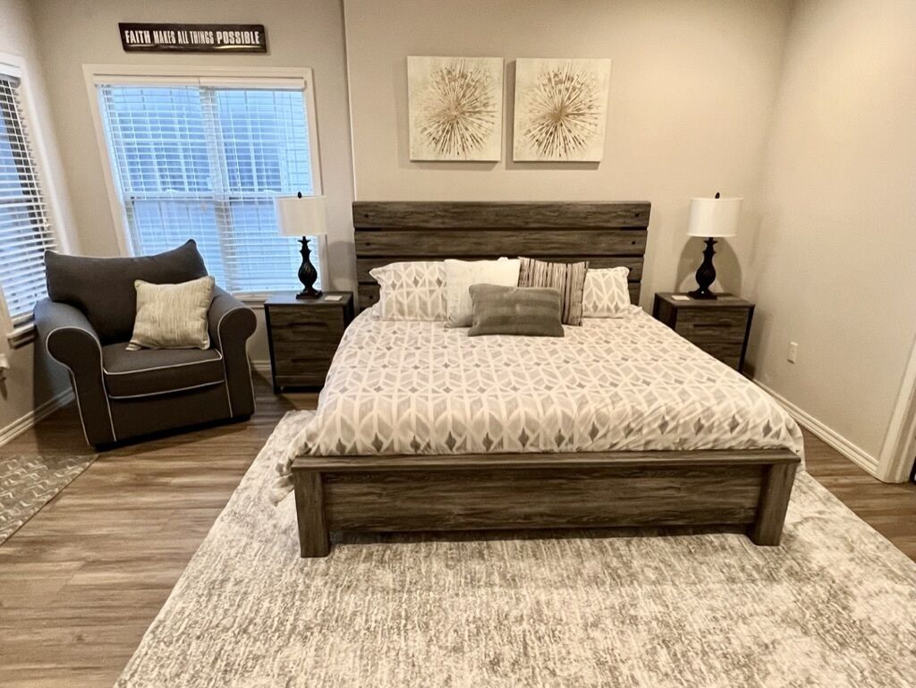 Une chambre à coucher avec un grand lit, une table de chevet, une chaise et une fenêtre avec des stores.