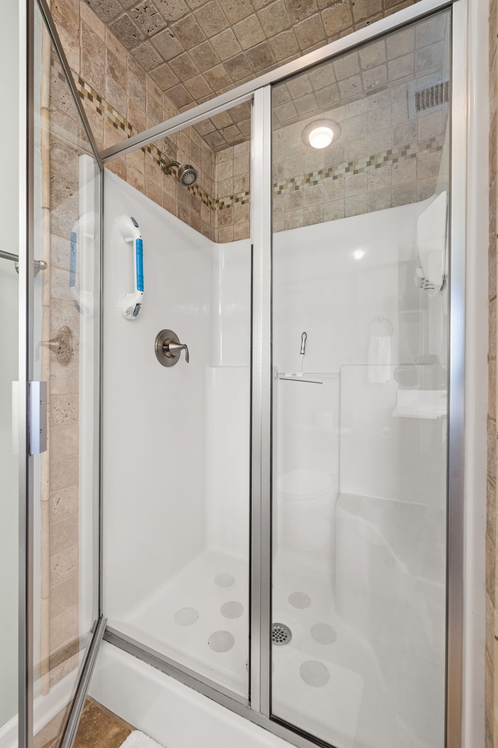A glass-enclosed shower with a tiled ceiling and a white wall.