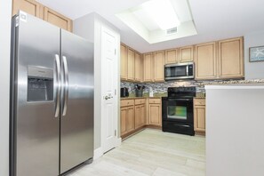 A modern kitchen with stainless steel appliances, wooden cabinets, a microwave, and a tiled backsplash. - Refreshing resort condo w/private balcony & amenities! 🌴 (Destin)