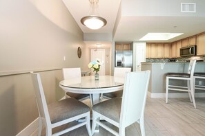 A modern kitchen with stainless steel appliances, a round dining table with chairs, and a small island with seating. - Refreshing resort condo w/private balcony & amenities! 🌴 (Destin)