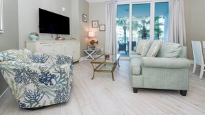 Een woonkamer met een bank, een salontafel, een televisie en een balkon met uitzicht op palmbomen.
