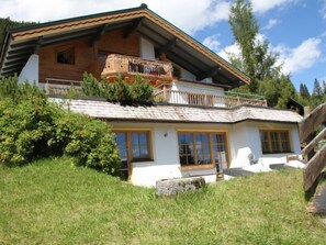Una chalet a due piani con un balcone, rivestimento in legno e fondamenta in pietra.