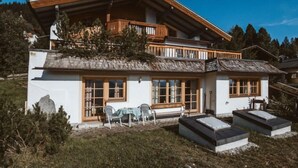 Un chalet à deux étages doté d’un balcon en bois, de grandes fenêtres et d’une cheminée en pierre.