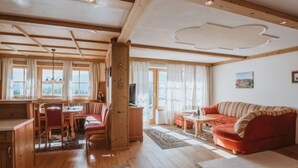 Un vaste espace de vie doté d’un plafond en bois, d’un canapé rouge, d’une table à manger avec des chaises et de grandes fenêtres offrant une vue sur l’extérieur.