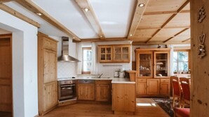 Un intérieur en bois comprenant une cuisine et un coin repas, avec des meubles de rangement en bois, une cuisinière et une table à manger avec des chaises.