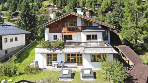 Un chalet à deux étages doté d’un balcon, situé dans une zone montagneuse boisée.