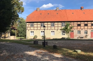 A traditional half-timbered building with a red-tiled roof, a cobblestone courtyard, and a small tree in the foreground. - Apartment on the Rittergut Bömitz (Bömitz)