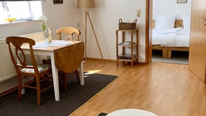 Une pièce comprenant une table à manger, des chaises, une lampe, une bibliothèque et un lit.