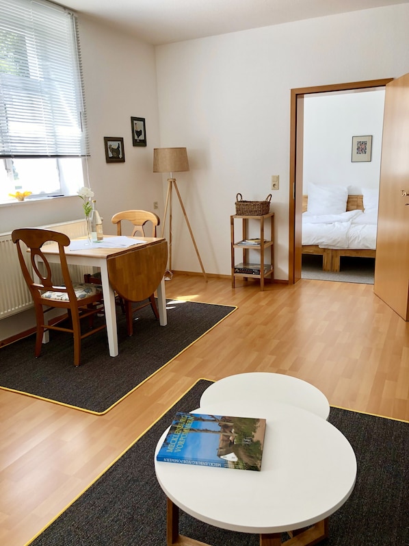 A room with a dining table, chairs, a lamp, a bookshelf, and a bed. - Apartment on the Rittergut Bömitz (Bömitz)