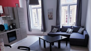 Moderni olohuone, jossa on harmaa sohva, musta sohvapöytä ja ruokailutila, jossa on valkoinen pöytä ja tuolit.