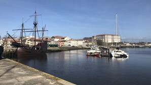 A harbor with a large sailing ship docked, smaller boats, and buildings along the waterfront.