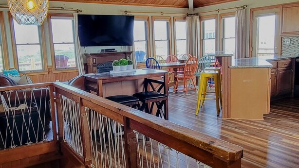 A spacious room with wooden floors, a balcony with a rope barrier, and a large window overlooking the outside. - WHO IS READY FOR SUNSHINE AND SAND?!  PACK YOUR SENSE OF ADVENTURE & COME VISIT! (Corolla)
