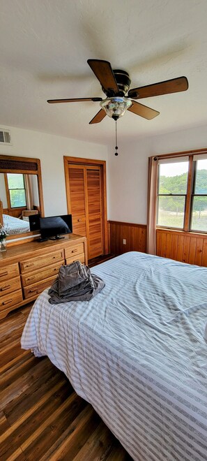 A bedroom with a bed, wooden dresser, television, and a ceiling fan.
