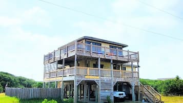 A multi-story building with a balcony, a staircase, and a vehicle parked in front.