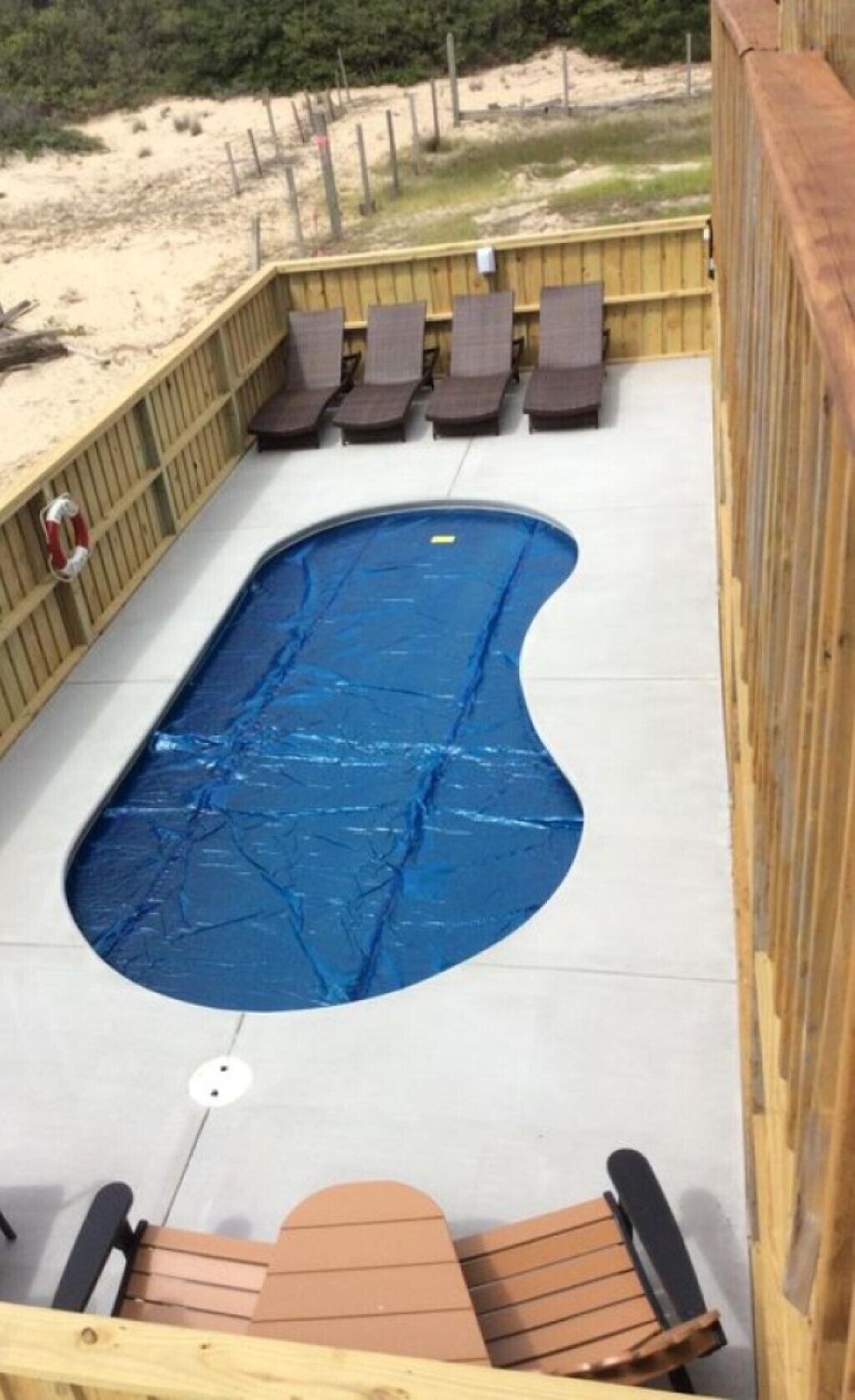 A pool area with a blue pool, wooden deck, and lounge chairs.