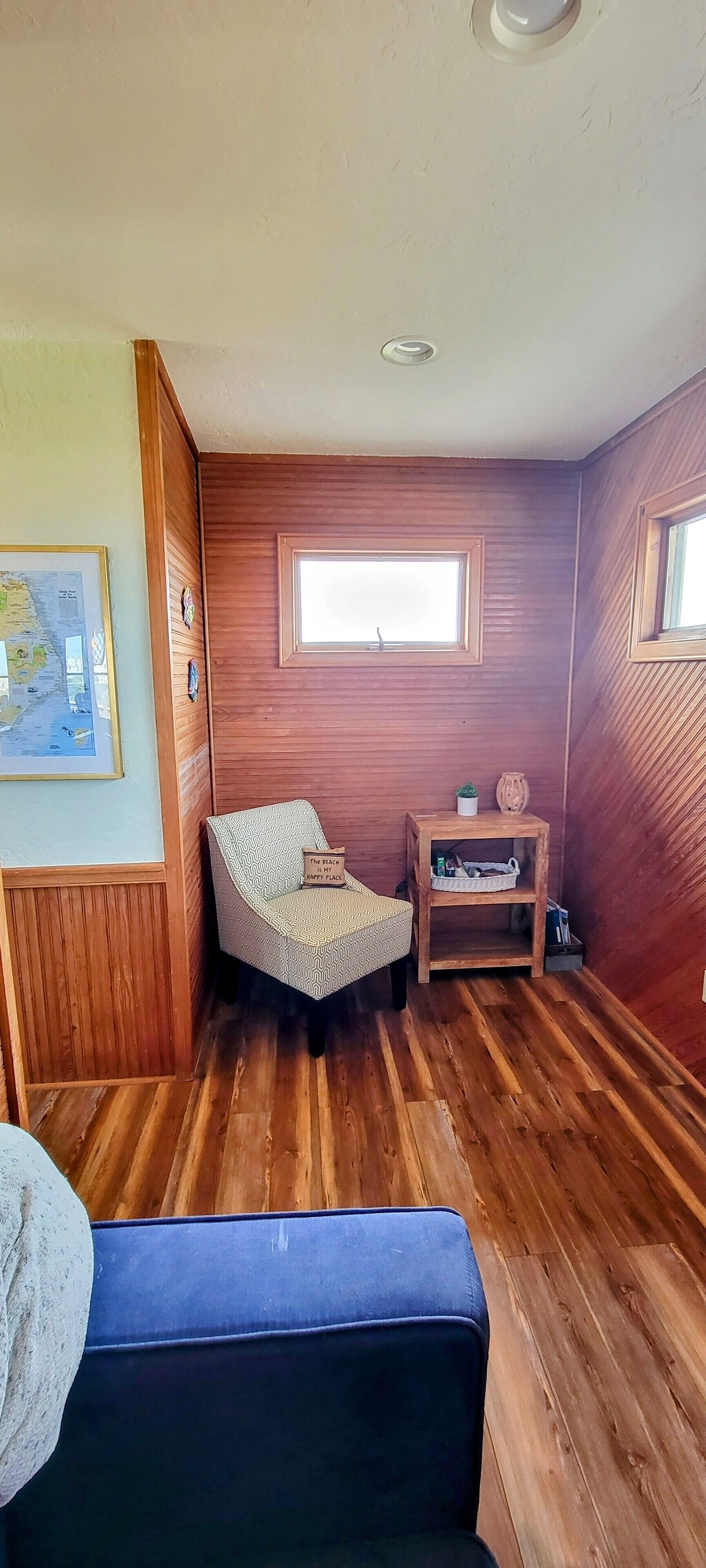A room with wooden paneling, a bed, a small table with a plant, and a framed map on the wall.