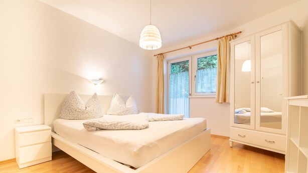 Un dormitorio con cama, mesitas de noche, un armario y una ventana con cortinas.