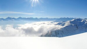 Un paisaje montañoso cubierto de nieve, con cielo despejado y el sol brillando intensamente.