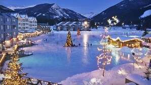 Ein verschneiter Stadtplatz mit einem geschmückten Weihnachtsbaum, Gebäuden und Bergen im Hintergrund.