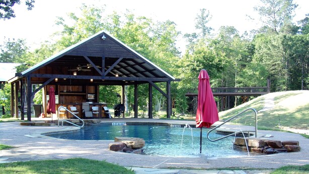 Un espace piscine abrité, agrémenté d’un pavillon en bois, d’un parasol rouge et d’un chemin de pierre menant à la piscine.
