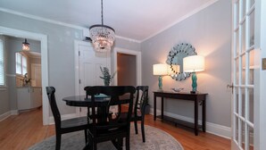 A dining area with a chandelier, a round table, and chairs. There is a mirror with a decorative frame on the wall, and a lamp on a side table. - Luxury on Main / North (Richmond)