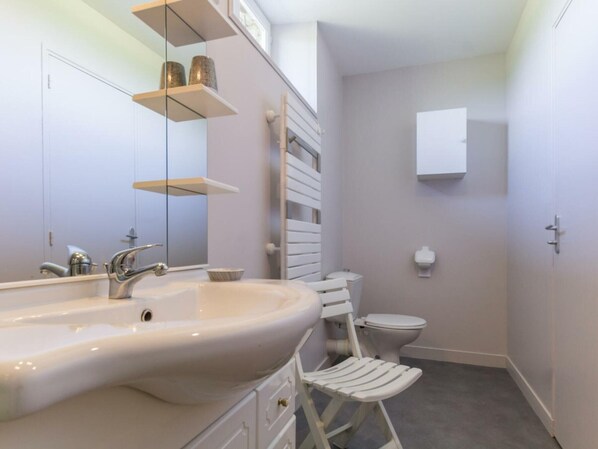 Un baño moderno con un lavamanos grande, un inodoro y un bidé. Hay repisas sobre el lavamanos y un espejo en la pared.