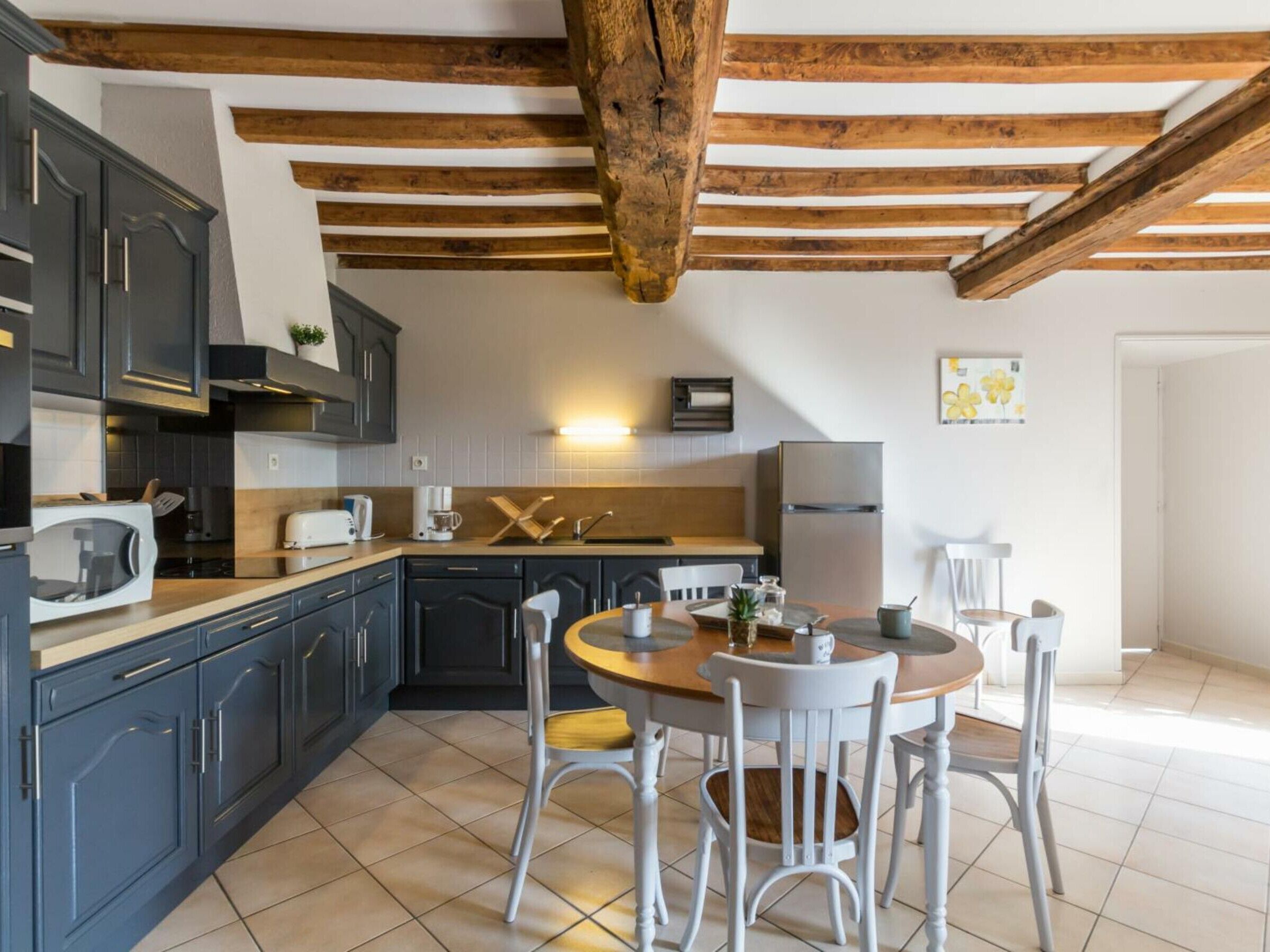 Una cocina moderna con armarios oscuros, techo de madera y un comedor con sillas blancas y una mesa de madera.