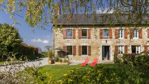 A stone building with a garden and two red lounge chairs in front.