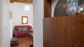 Uma sala de estar acolhedora com um sofá vermelho, uma mesa de centro de madeira e um vaso estampado sobre um armário de madeira.