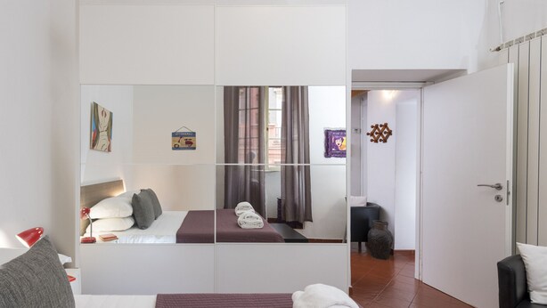 Quarto de hotel com cama, espelho grande, guarda-roupa, escrivaninha e cadeira.