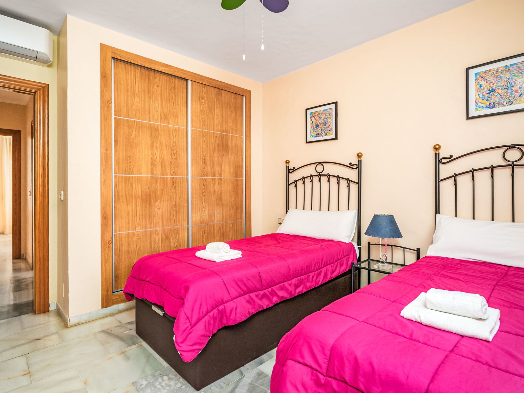 A bedroom with two beds, a wooden wardrobe, and a ceiling fan.