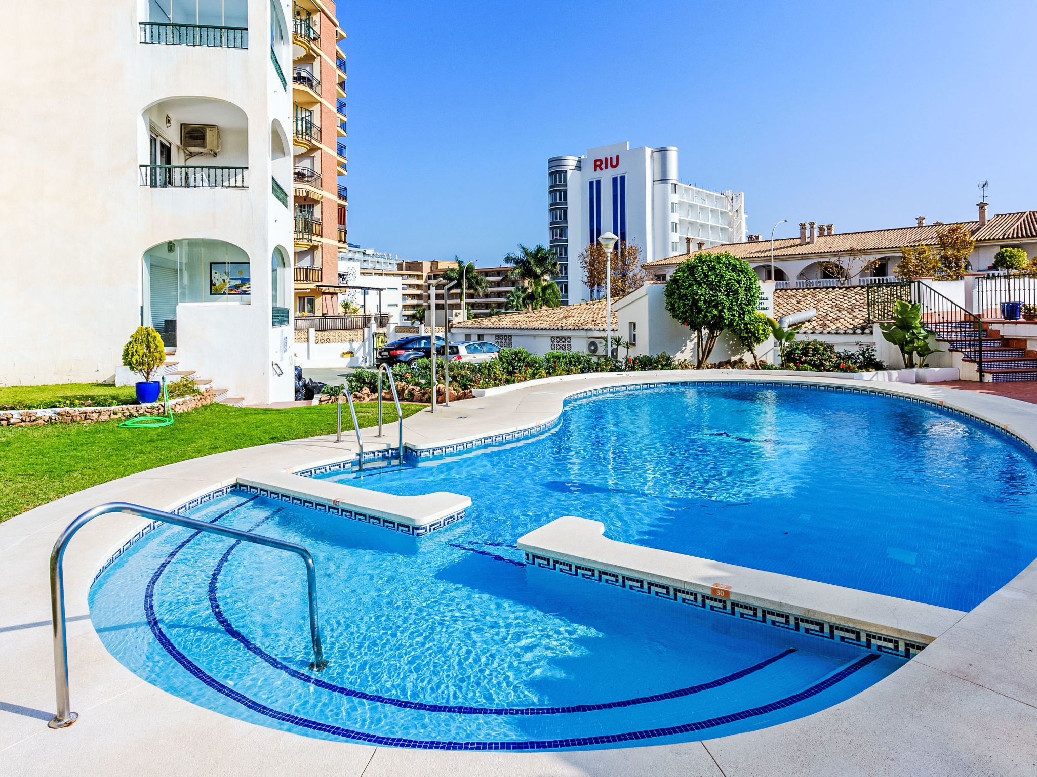 Una piscina con diseño curvo, rodeada por un césped bien cuidado y un edificio con balcones.