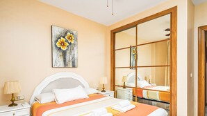 Ein Hotelzimmer mit einem großen Bett, einem Nachttisch mit Lampe, einem Gemälde an der Wand und einem großen Spiegel.