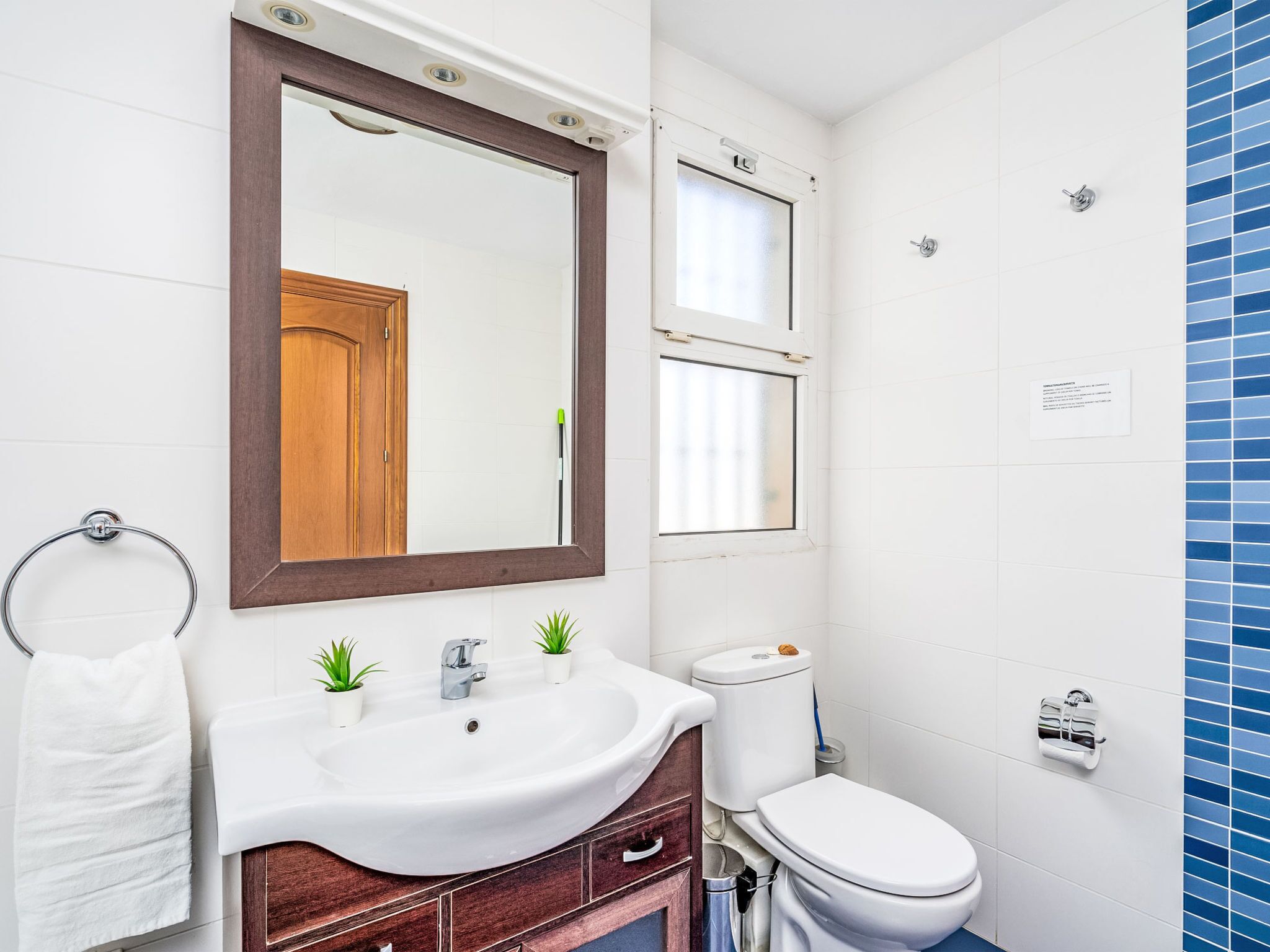 Un baño moderno con un lavamanos blanco, tocador de madera y un espejo grande.
